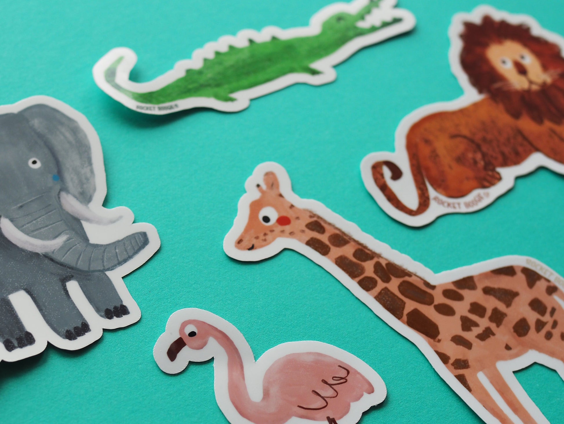 Set of animal stickers including elephant, crocodile, lion, giraffe, and flamingo on a turquoise background.