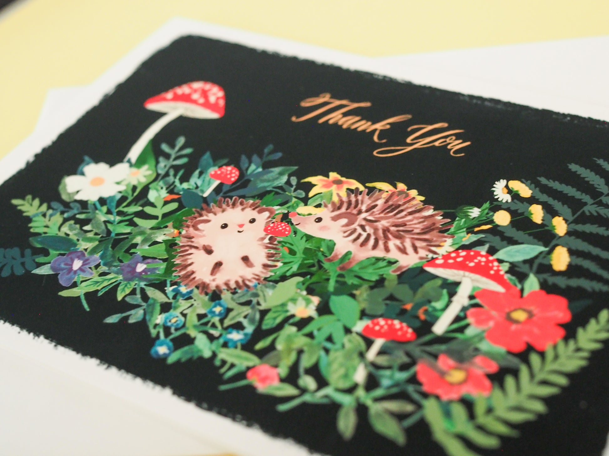 Greeting card with hedgehog, flowers, and mushrooms on a black background