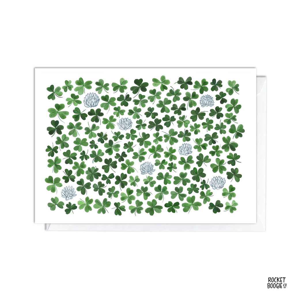 A greeting card featuring a pattern of green clovers and silver accents on a premium cardstock surface.