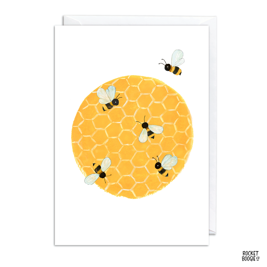 A greeting card with a yellow honeycomb pattern and illustrations of bees on it. The card is folded and has a white envelope behind it.