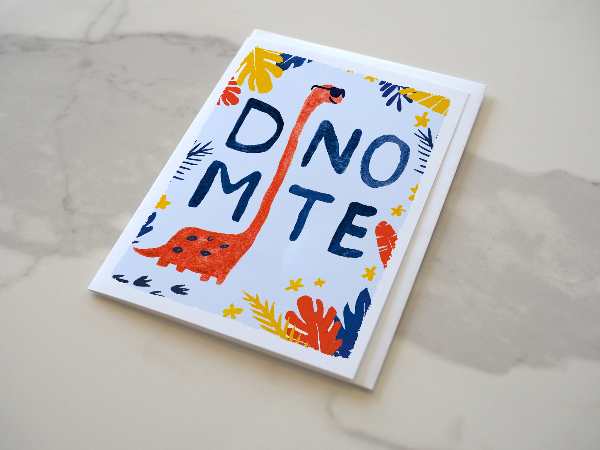 Card with dinosaur illustration and 'DINO MITE' text on a marble surface